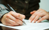 close up of a person's hands writing on a document