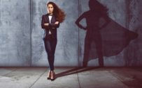 A woman stands in front of a wall with a superhero shadow behind her.