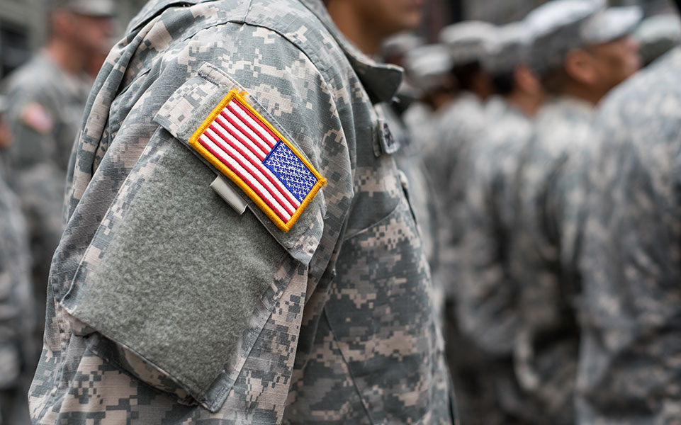 A soldier stands in uniform, bearing the American flag patch.