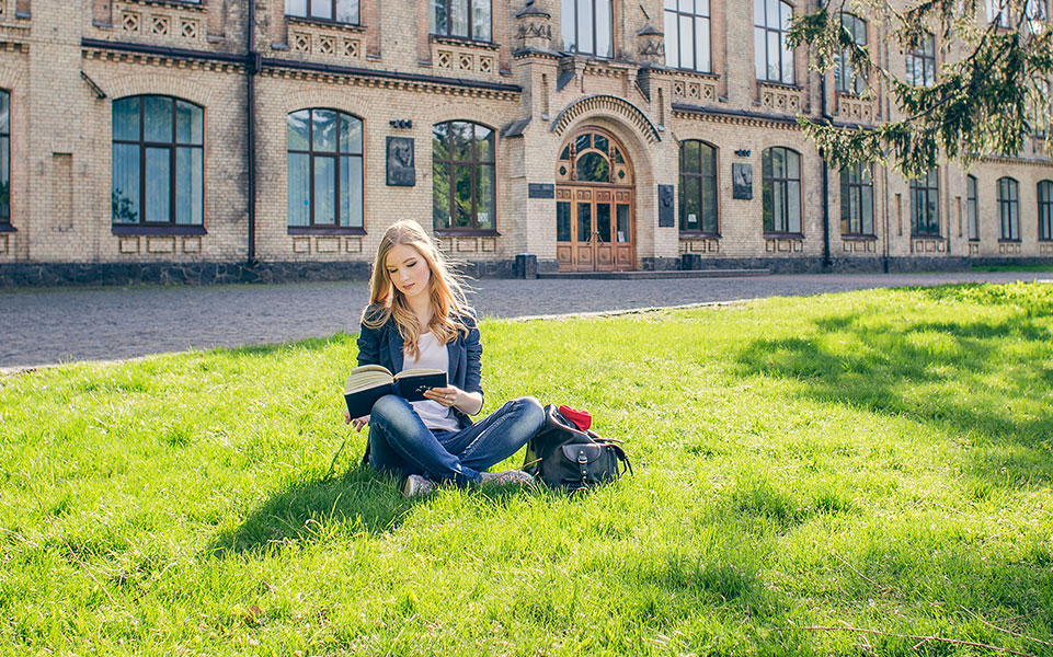 A college student reads a book on the campus lawn.