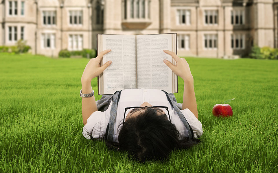 A philosophy student reads a book on the campus lawn.