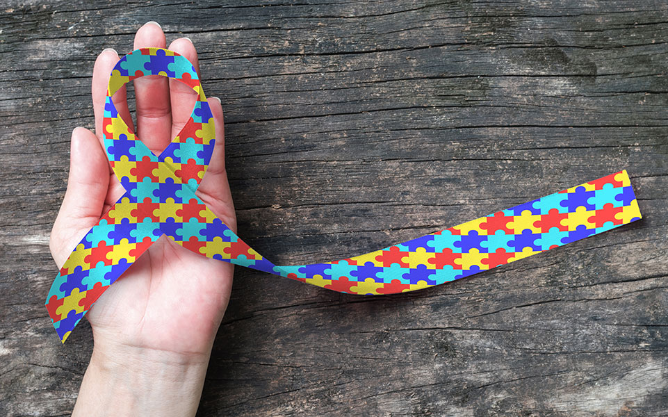 A hand holds the Autism Awareness Ribbon.