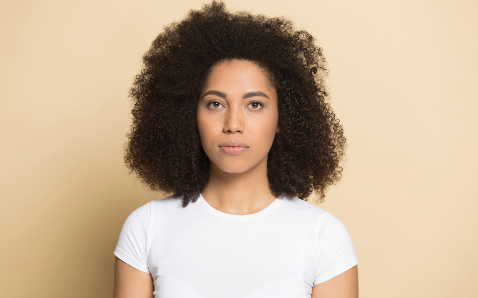 A woman of color stands against a plain background.
